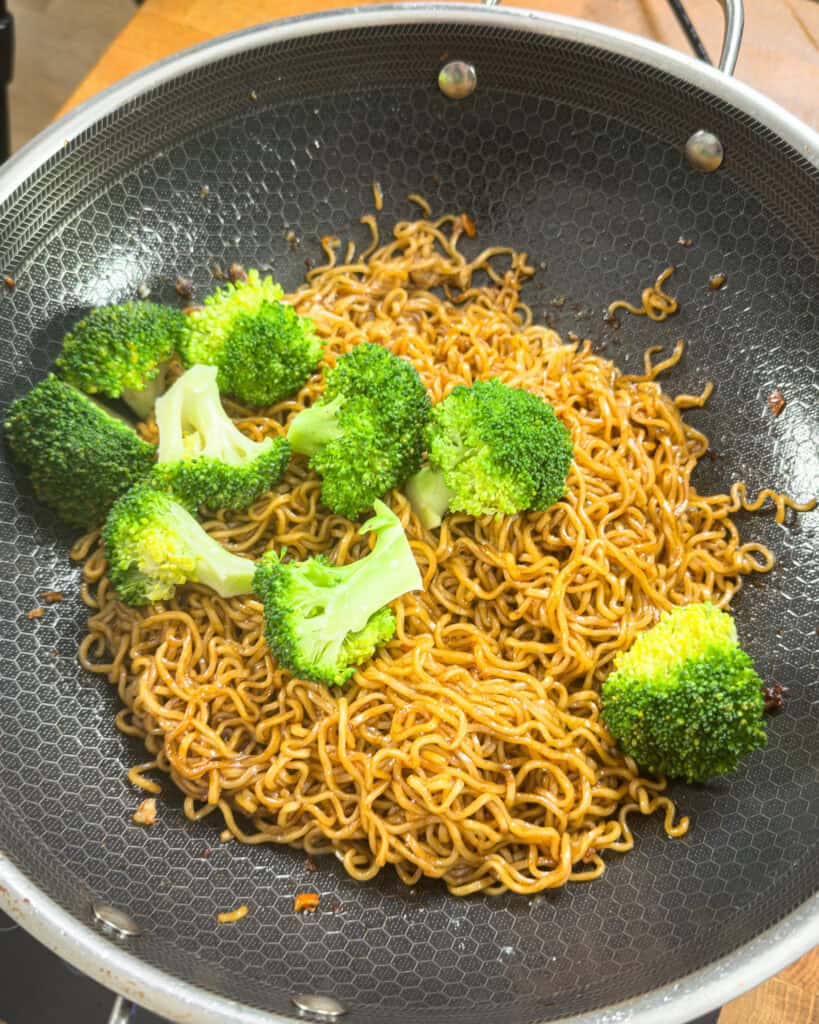 Sauced noodles and broccoli in a black pan for Beef and Broccoli Chow Mein - GENIUS EATS Sauced noodles and broccoli in a black pan for Beef and Broccoli Chow Mein