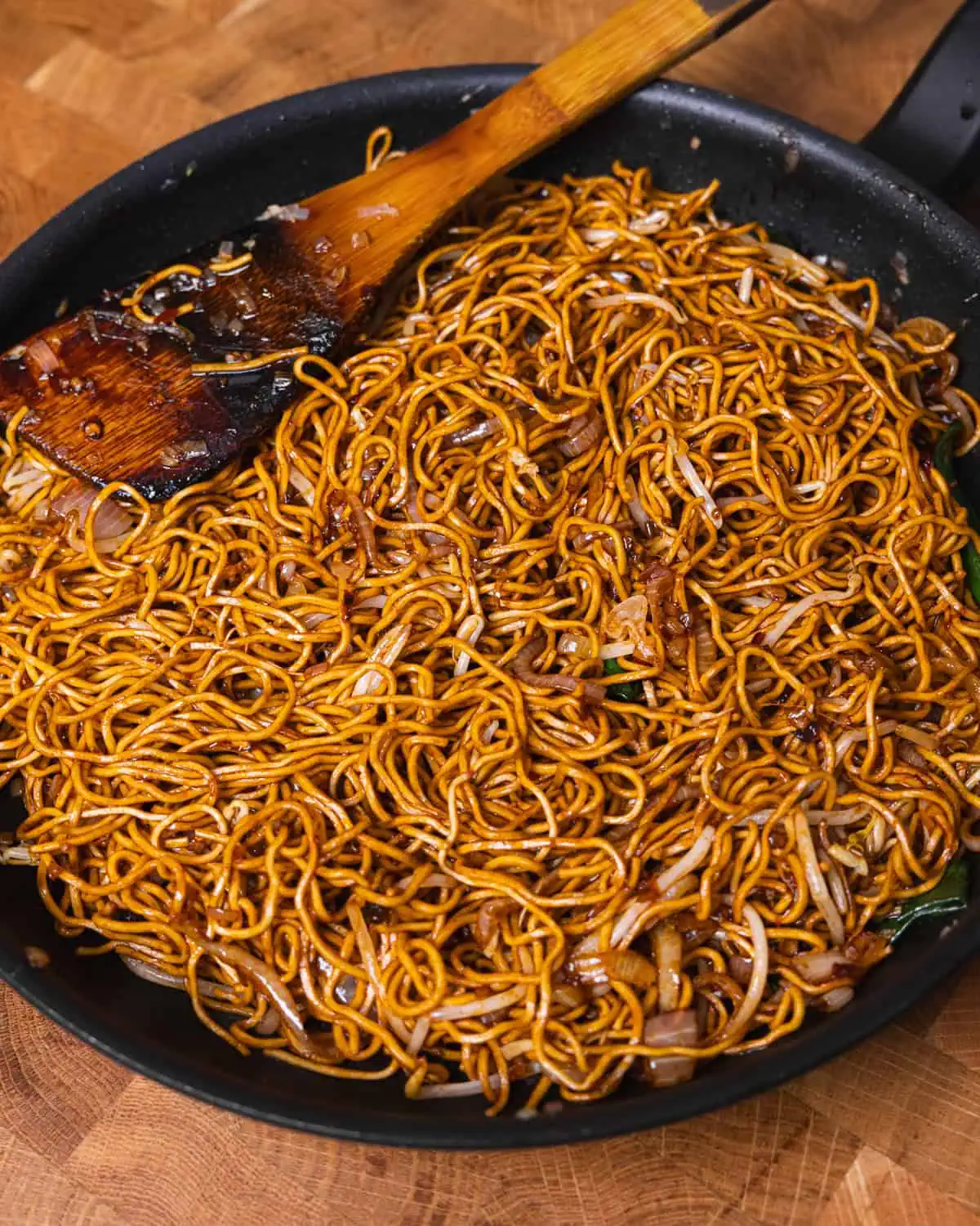 Chili Oil Soy Sauce Chow Mein tossed in a pan with a wooden spatula - GENIUS EATS Chili Oil Soy Sauce Chow Mein being tossed in a pan with a wooden spatula